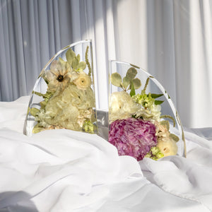 Resin bookends featuring preserved wedding flowers in soft ivory, pale yellow, and plum tones, elegantly displayed on white fabric with sunlight casting soft shadows.