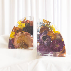 Arched pair of resin bookends with preserved yellow ranunculus, purple anemone, rust roses, and blue delphinium from a wedding bouquet