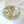 Crystal-clear resin jewelry dish with preserved green botanicals and eucalyptus embedded throughout, holding a diamond engagement ring set and gold wedding band, displayed on white fabric