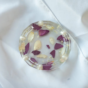Round resin jewelry dish with faceted edges, featuring preserved purple and cream flower petals, tiny blooms, and pearl accents — wedding keepsake by Everlasting Bloom Co.