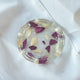 Round resin jewelry dish with faceted edges, featuring preserved purple and cream flower petals, tiny blooms, and pearl accents — wedding keepsake by Everlasting Bloom Co.