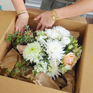 Everlasting Bloom Co team member carefully packing a wedding bouquet with white dahlias and peach roses into a Bloom Box shipping kit
