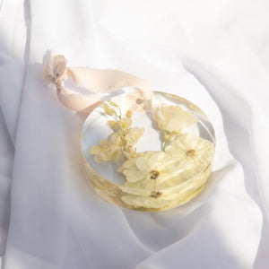 Round ornament with a blush silk ribbon, featuring ivory spray roses and ivory larkspur from a wedding bouquet