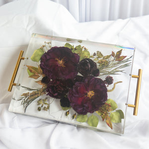 Rectangular clear resin floral tray with gold handles, holding preserved deep burgundy roses, eucalyptus, and trailing greenery from a wedding bouquet.