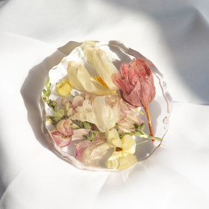 Geode-shaped resin coaster with preserved pink tulip, cream tulip, pink snapdragons, and pale yellow florets from a wedding bouquet