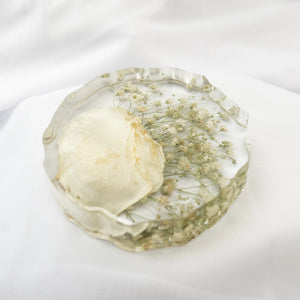 Round resin geode coaster with organic ruffled edge, holding a preserved white rose petal and baby's breath from a wedding bouquet.