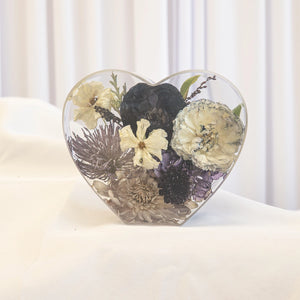 Heart-shaped resin keepsake with preserved black rose, ivory carnations, purple thistle, and cream chrysanthemum from a wedding bouquet