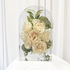 Large arch-shaped clear resin piece with preserved white roses, baby's breath, and eucalyptus greenery displayed on a white surface