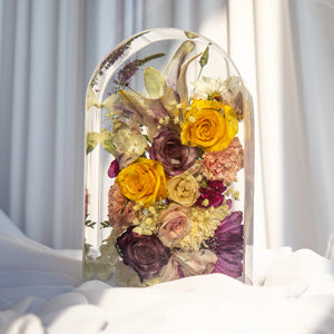 Large clear resin arch keepsake with preserved yellow roses, purple roses, blush carnations, and baby's breath from a wedding bouquet.