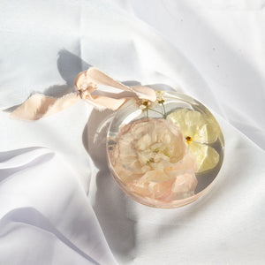 Round resin ornament with peach silk ribbon, preserved blush peony, yellow buttercup, and white chamomile from a wedding bouquet
