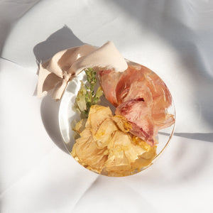 Round resin ornament with peach silk ribbon, preserved coral garden rose, butter yellow rose, and bells of Ireland from a wedding bouquet