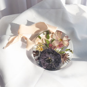 Round resin ornament with peach silk ribbon, preserved eggplant anemone, blush anemone, cream chamomile, and burgundy scabiosa from a wedding bouquet