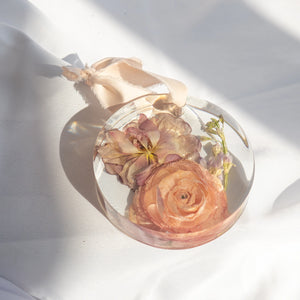Round resin ornament with peach silk ribbon, preserved peach ranunculus, mauve lily, and lavender delphinium from a wedding bouquet