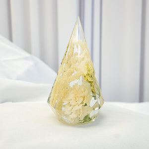 Faceted teardrop resin ring holder with preserved ivory and white wedding flowers and greenery suspended inside.