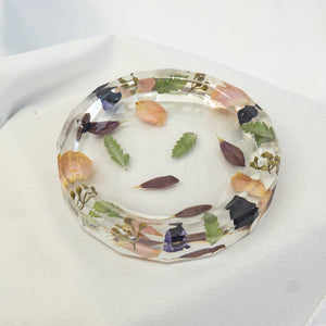 Octagonal clear resin jewelry dish with pressed greenery, leaves, and blush and deep purple flower petals around the rim.