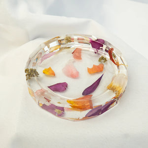 Octagonal clear resin jewelry dish with pressed purple, pink, orange, and yellow flower petals embedded around the rim.