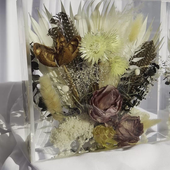 Panning video of an 8x8 resin flower preservation block featuring dried florals, pampas grass, preserved mauve rose, yellow strawflowers, feathers, and a butterfly — handmade memorial or wedding keepsake in clear epoxy