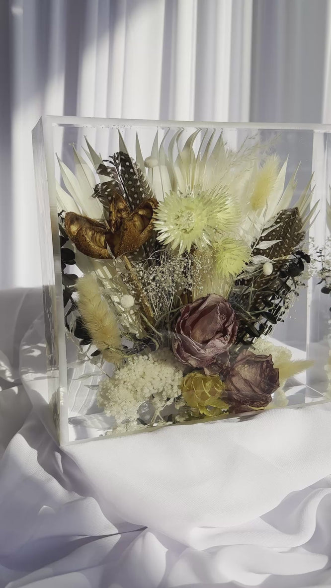 Panning video of an 8x8 resin flower preservation block featuring dried florals, pampas grass, preserved mauve rose, yellow strawflowers, feathers, and a butterfly — handmade memorial or wedding keepsake in clear epoxy