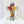 Clear resin cross with preserved pink, yellow, and orange roses, blue delphinium, and greenery, displayed upright on white fabric