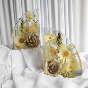 Set of curved resin bookends featuring preserved ivory roses, daisies, and delicate filler flowers from a wedding bouquet, styled on white fabric.