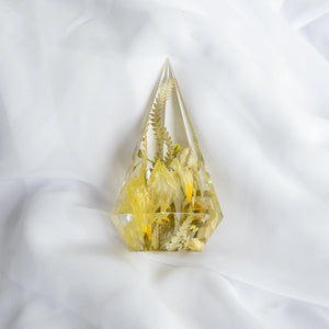 Faceted resin ring holder with preserved yellow flowers and ferns, resting on white fabric background.