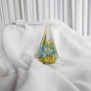 Faceted resin ring holder with preserved blue flowers and gold flakes, styled on soft white fabric.