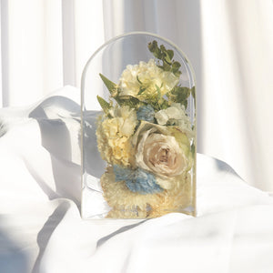 Small arch with an ivory rose, ivory carnations, a white chrysanthemum, blue hydrangea, baby's breath, and greenery from a wedding bouquet