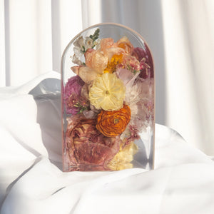 Small arch with orange and yellow ranunculus, mauve and peach garden roses, a magenta ranunculus, a blush peony, pink stock, and white snapdragons from a wedding bouquet
