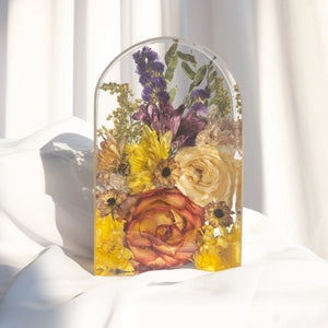 Small arch with a bicolor orange rose, an ivory rose, yellow chrysanthemums, bronze daisies, burgundy alstroemeria, purple statice, and yellow solidago from a wedding bouquet