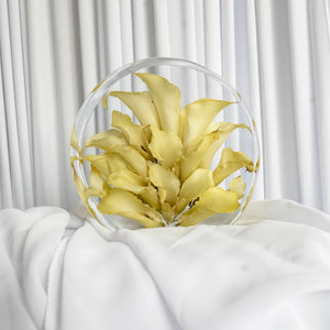 Small resin standing circle with preserved yellow calla lily petals, arranged in a sculptural bloom and styled on soft white fabric.