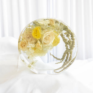 Standing circular resin display with preserved cream roses, yellow lisianthus, white hydrangea, and trailing green amaranthus from a wedding bouquet
